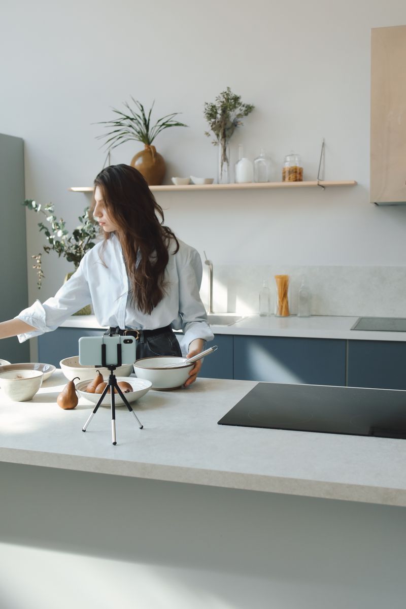Woman preparing food while filming a cooking video in a stylish, modern kitchen setting.